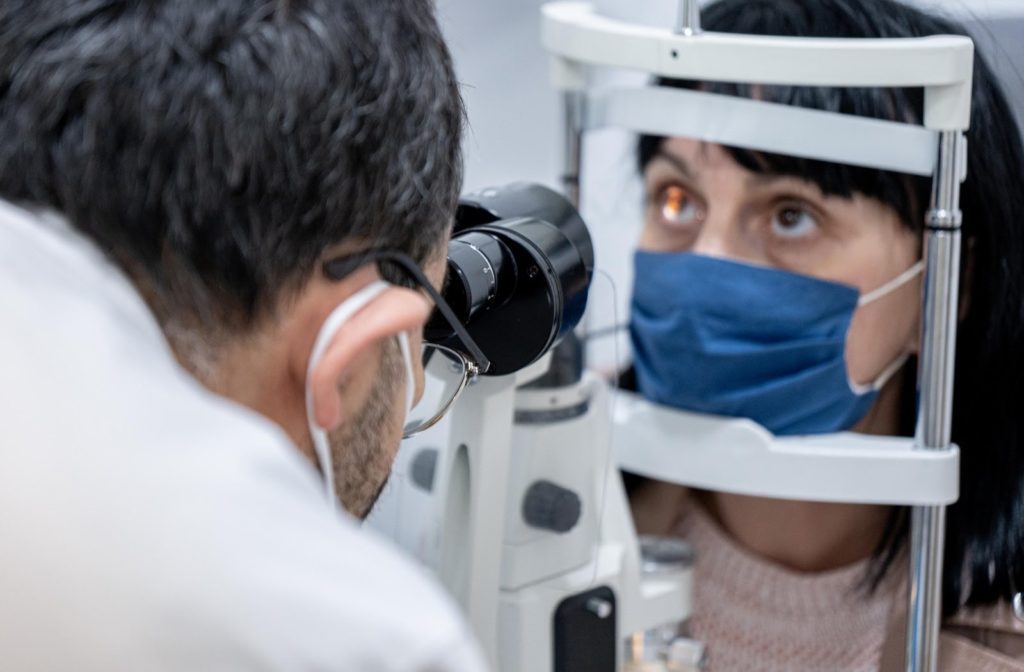An optometrist conducting an eye examination while both wear face masks