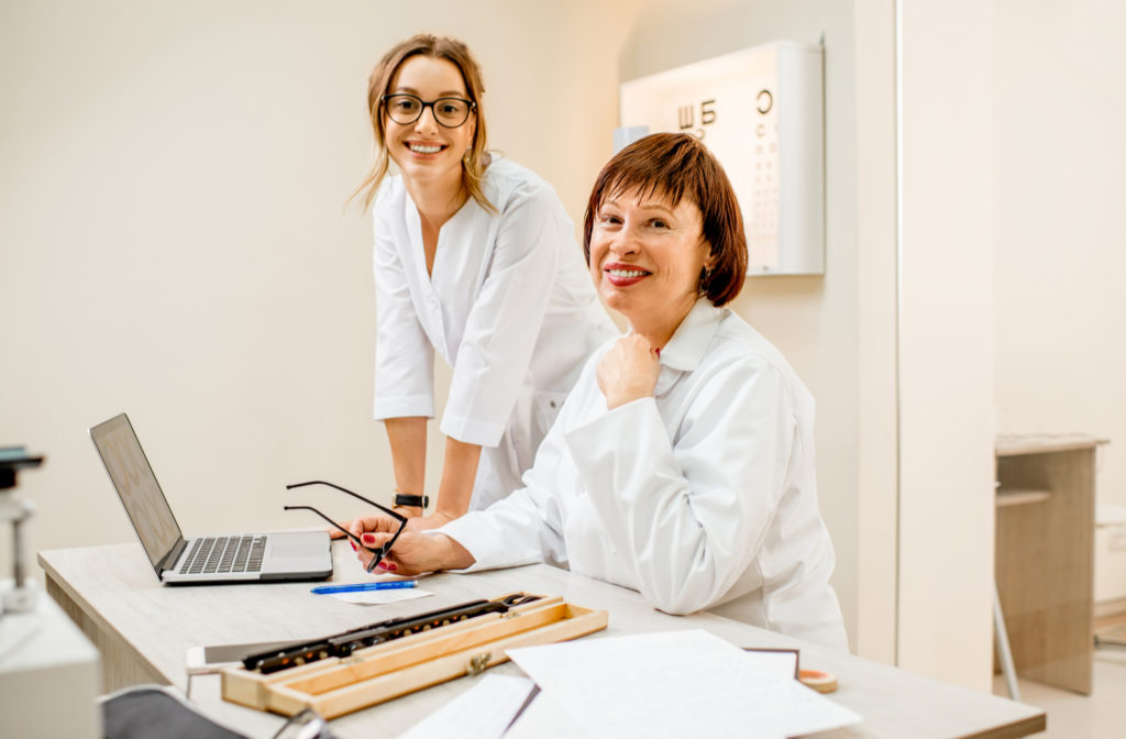 Senior female optometrist with young female assistant working with laptop at the office