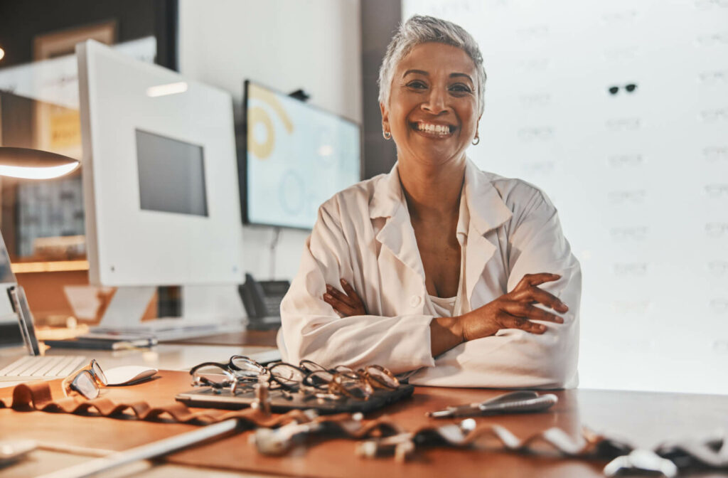 an optician smiles and sits behind her desk with several pairs of frames on the table