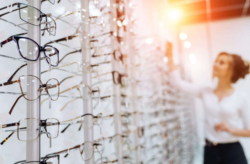 an optician organizes frames on a wall in an optical. She is standing at the back of the image, out of focus